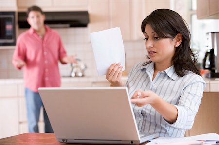 Woman in kitchen with paperwork using laptop with man in backgro Stock Photo - Budget Royalty-Free & Subscription, Code: 400-04043662
