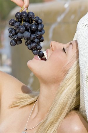 simsearch:400-04058311,k - A beautiful young blond woman sitting in front of a fountain eating a bunch of black grapes Foto de stock - Super Valor sin royalties y Suscripción, Código: 400-04054839