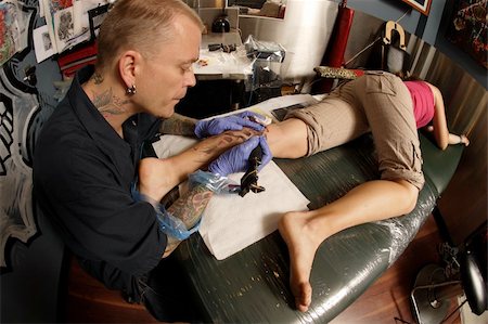 simsearch:400-04343139,k - A tattoo artist applying his craft onto the lower leg of a pain-inflicted female. Photographie de stock - Aubaine LD & Abonnement, Code: 400-04050918