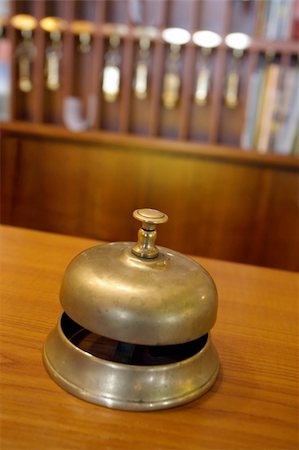 Vintage brass bell on hotel front desk with blurred key rack in the background. Very shallow depth of field with focus on the button. Stock Photo - Budget Royalty-Free & Subscription, Code: 400-04067288