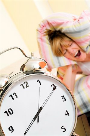 simsearch:6109-06194408,k - Close up of alarm clock. Young woman in the background covering ears with pillow. Stockbilder - Microstock & Abonnement, Bildnummer: 400-04067346