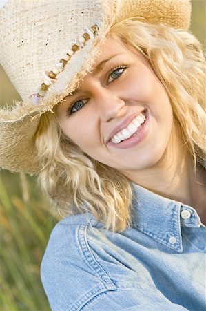 simsearch:400-04058311,k - A beautiful blond haired blue eyed model wearing a straw cowboy hat sits amid tall grass illuminated by golden evening sunlight Foto de stock - Super Valor sin royalties y Suscripción, Código: 400-04069557
