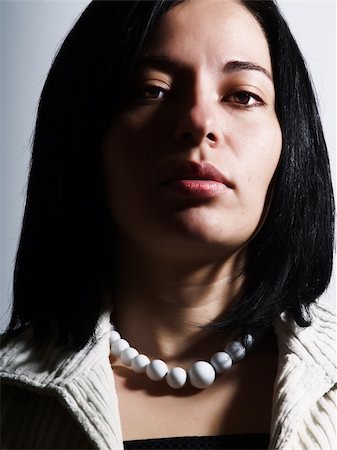 A high-key portrait about an attractive lady with black hair who is looking ahead and she has a glamorous look. She is wearing a white coat, a black dress and a white necklace. Photographie de stock - Aubaine LD & Abonnement, Code: 400-04060043