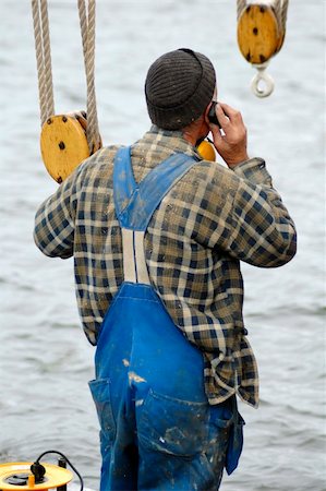 dirty overalls pictures - A sailor, engaged in boat maintenance whilst in port, takes a break to make a phone call on his mobile phone. Stock Photo - Budget Royalty-Free & Subscription, Code: 400-04060065