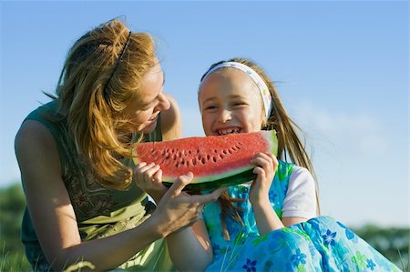 simsearch:400-06177351,k - Happy young girl eating watermelon at meadow with shes mother Stock Photo - Budget Royalty-Free & Subscription, Code: 400-04082519
