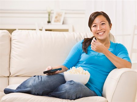 Beautiful Asian woman sitting on the couch eating popcorn with the remote in her hand. Horizontally framed photo. Stock Photo - Budget Royalty-Free & Subscription, Code: 400-04119207