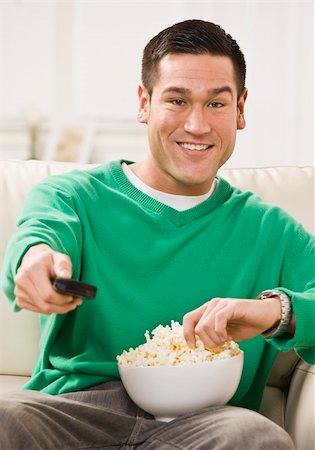 Attractive Asian man sitting on a sofa with popcorn and a remote control. Vertically framed photo Stock Photo - Budget Royalty-Free & Subscription, Code: 400-04119209
