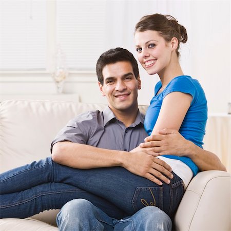 An attractive young couple relaxing together in their home.  The woman is sitting on the man's lap and they are smiling at the camera happily. Square composition. Stock Photo - Budget Royalty-Free & Subscription, Code: 400-04119251