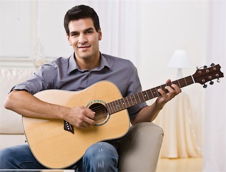 An attractive and relaxed looking man sitting on a couch and playing the guitar.  He is smiling at the camera. Horizontally framed shot. Stock Photo - Budget Royalty-Free & Subscription, Code: 400-04119253
