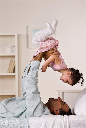 A man is laying on a bed and holding up his baby daughter.  They are smiling at each other.  Vertically framed shot. Stock Photo - Budget Royalty-Free & Subscription, Code: 400-04124075