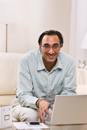 A man is seated in his living room and is working on a laptop.  He is smiling at the camera.  Vertically framed shot. Stock Photo - Budget Royalty-Free & Subscription, Code: 400-04124078