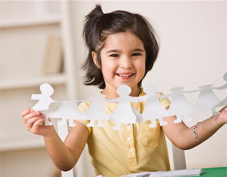 A young girl is seated at a desk and is holding up paper dolls.  She is smiling at the camera.  Horizontally framed shot. Stock Photo - Budget Royalty-Free & Subscription, Code: 400-04124071