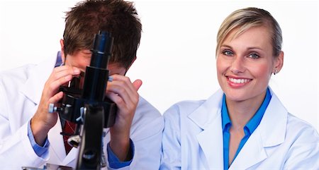 simsearch:400-05669818,k - Beautiful woman smiling at the camera and male scientist looking through a microscope Fotografie stock - Microstock e Abbonamento, Codice: 400-04125252