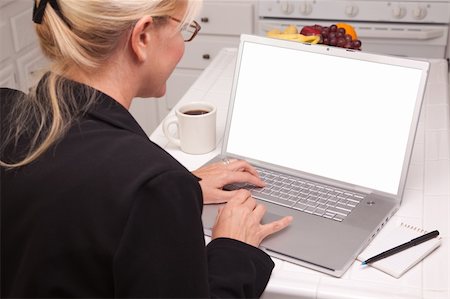 simsearch:400-06857713,k - Woman Sitting In Kitchen Using Laptop with Blank Screen. Screen can be easily used for your own message or picture using the included clipping path. Fotografie stock - Microstock e Abbonamento, Codice: 400-04125357