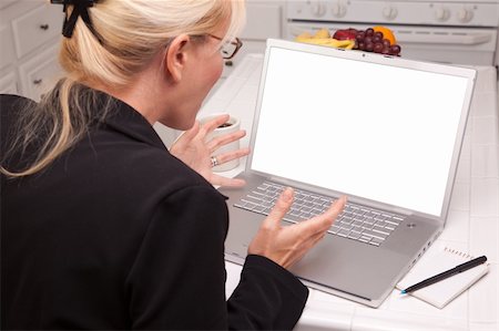 simsearch:400-05129327,k - Woman Sitting In Kitchen Using Laptop with Blank Screen. Screen can be easily used for your own message or picture using the included clipping path. Stock Photo - Budget Royalty-Free & Subscription, Code: 400-04125359