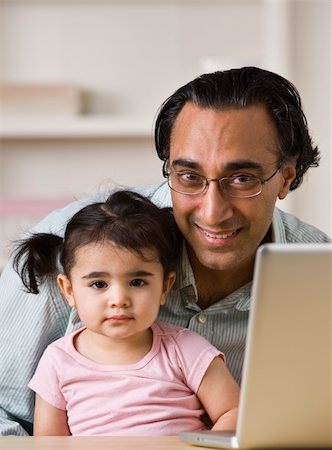 An Indian father holds his young daughter.  He is smiling directly at the camera. There is a laptop on the table. Vertically framed shot. Stock Photo - Budget Royalty-Free & Subscription, Code: 400-04126324