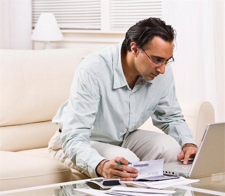A man paying his bills online.  He has a checkbook in his hand.  Square framed shot. Stock Photo - Budget Royalty-Free & Subscription, Code: 400-04126328