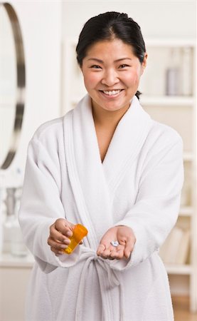 A woman is standing in her bathroom and holding a bottle of medication.  She is showing some pills to the camera and smiling.  Vertically framed shot. Stock Photo - Budget Royalty-Free & Subscription, Code: 400-04126340