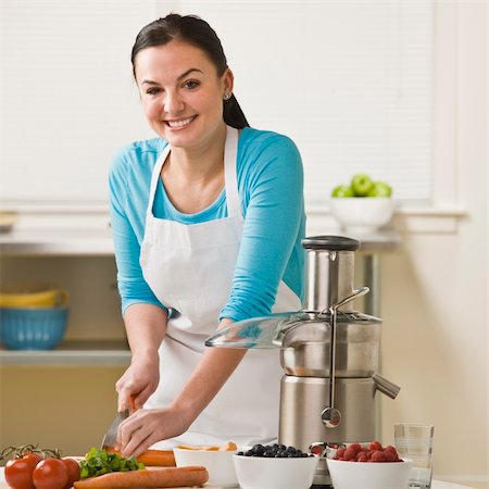 A woman is in the kitchen and slicing produce for the juicer.  She is smiling at the camera.  Square framed shot. Stock Photo - Budget Royalty-Free & Subscription, Code: 400-04126354