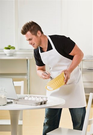 Attractive male cooking with mixing bowl and looking at laptop. Vertical Stock Photo - Budget Royalty-Free & Subscription, Code: 400-04126387