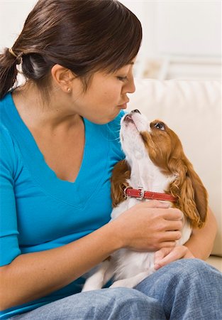 A young woman holding a dog on her lap and making a kissing gesture. She has dark brown hair. Vertically framed photo. Stock Photo - Budget Royalty-Free & Subscription, Code: 400-04120530