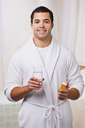 An attractive young man holding a prescription bottle and glass of water.  He is wearing a bathrobe and is smiling at the camera. Vertically framed photo. Stock Photo - Budget Royalty-Free & Subscription, Code: 400-04120562