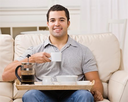 An attractive young man eating from a breakfast tray.  He has a coffee cup raised, and is smiling directly at the camera.  Horizontally framed photo. Stock Photo - Budget Royalty-Free & Subscription, Code: 400-04120605