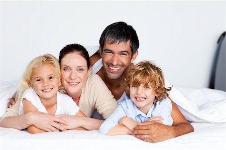 simsearch:400-04192370,k - Smiling family lying together on bed Fotografie stock - Microstock e Abbonamento, Codice: 400-04121408
