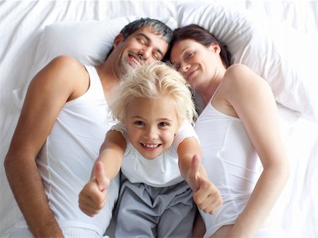 simsearch:400-04192370,k - Happy little girl on bed with thumbs up smiling at the camera and her parents Fotografie stock - Microstock e Abbonamento, Codice: 400-04123054