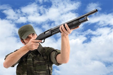 simsearch:400-05364066,k - Un homme (soldat, chasseur, guérilla, etc.) portant un vêtement de camouflage vise avec son fusil à pompe et un fond de ciel nuageux. Photographie de stock - Aubaine LD & Abonnement, Code: 400-04130849