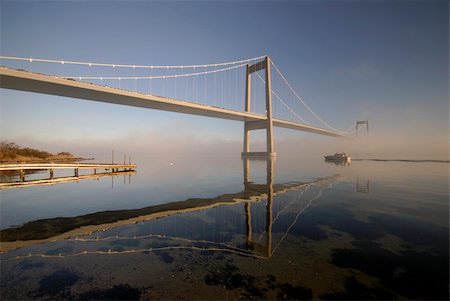 fun - Beautiful suspension bridge and one boat sailing.  Sunny blue and cold foggy day in Denmark. Foto de stock - Super Valor sin royalties y Suscripción, Código: 400-04132187