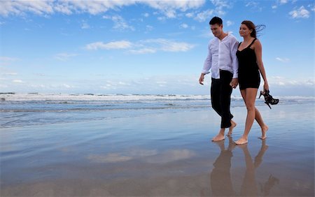 simsearch:400-06751687,k - A beautiful romantic young man and woman couple walking hand in hand and barefoot on a beach. They are dressed as if it is after a night out and the girl is carrying her shoes. Stock Photo - Budget Royalty-Free & Subscription, Code: 400-04148926
