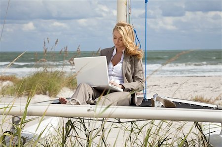 A beautiful young woman in a smart suit sitting barefoot on the deck of a small catamaran sailing boat using her laptop computer with the beach and sea behind her Stock Photo - Budget Royalty-Free & Subscription, Code: 400-04149268