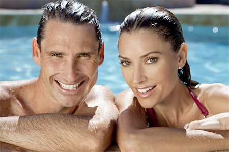 Close up portrait of a beautiful happy man and woman couple resting on their hands at the side of a sun bathed swimming pool smiling with perfect teeth. Foto de stock - Super Valor sin royalties y Suscripción, Código: 400-04149660