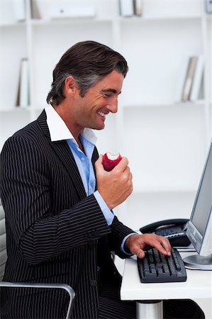 Happy businessman eating a red apple at his desk Stock Photo - Budget Royalty-Free & Subscription, Code: 400-04157305