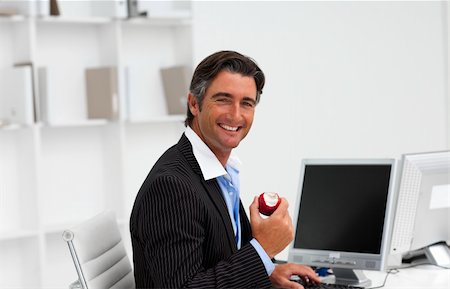 Businessman eating a fruit at work and smiling at the camera Stock Photo - Budget Royalty-Free & Subscription, Code: 400-04157306