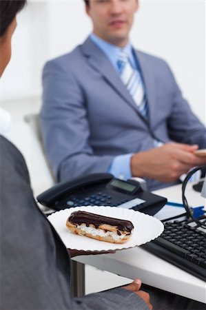 Close-up of a businesswoman carrying a pastry to her desk with her colleague in the background Stock Photo - Budget Royalty-Free & Subscription, Code: 400-04157413