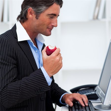 Close-up of a happy businessman eating a red apple in the office Foto de stock - Super Valor sin royalties y Suscripción, Código: 400-04157425