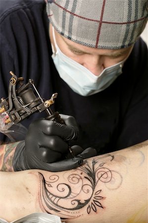A tattoo artist applying his craft onto the leg of a female. Fotografie stock - Microstock e Abbonamento, Codice: 400-04159771