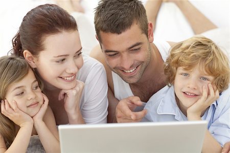 Portrait of family lying in bed using a laptop Stock Photo - Budget Royalty-Free & Subscription, Code: 400-04151159