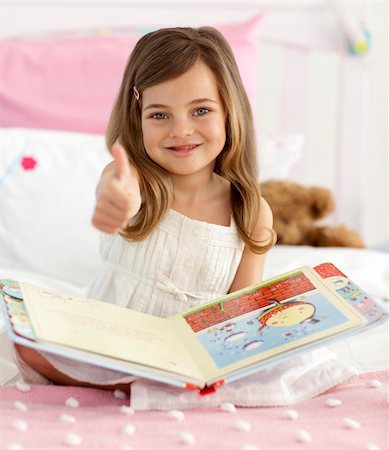 simsearch:400-06747549,k - Happy little girl reading a book sitting in bed with thumb up Foto de stock - Super Valor sin royalties y Suscripción, Código: 400-04151246