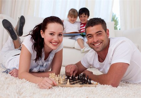 simsearch:400-04467628,k - Happy couple playing chess on floor in living-room with their children on sofa Photographie de stock - Aubaine LD & Abonnement, Code: 400-04152014