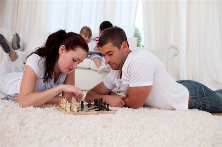 simsearch:400-04467628,k - Couple playing chess on floor in living-room with their children on sofa Photographie de stock - Aubaine LD & Abonnement, Code: 400-04152011