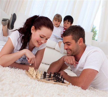 simsearch:400-04467628,k - Smiling couple playing chess on floor in living-room with their children on sofa Photographie de stock - Aubaine LD & Abonnement, Code: 400-04152013