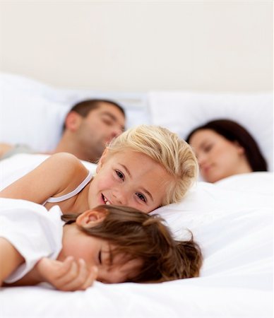Little girl smiling on bed wile her parents and brother sleep Stock Photo - Budget Royalty-Free & Subscription, Code: 400-04152117
