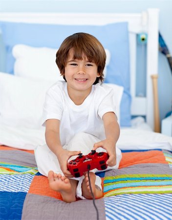 Little boy playing videogames sitting in his bed Stock Photo - Budget Royalty-Free & Subscription, Code: 400-04152192