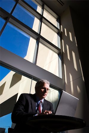 simsearch:400-04167566,k - Low angle view of a businessman with a laptop computer in front of large windows. Vertical shot. Stockbilder - Microstock & Abonnement, Bildnummer: 400-04164619