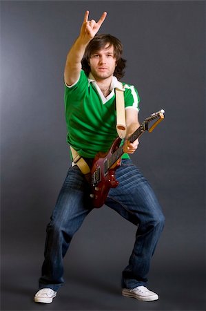 Portrait of a successful rockstar holding an electric guitar and making a rock sign on a dark background Stock Photo - Budget Royalty-Free & Subscription, Code: 400-04165969