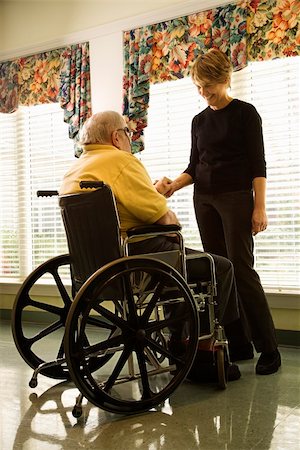 Elderly man in a wheelchair and a young woman stand by a window and hold hands.  Vertical shot. Stock Photo - Budget Royalty-Free & Subscription, Code: 400-04167945