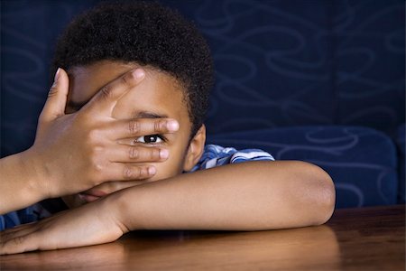 Young African American boy peeks through his fingers as he sits at a coffee table. Horizontal shot. Stock Photo - Budget Royalty-Free & Subscription, Code: 400-04168203